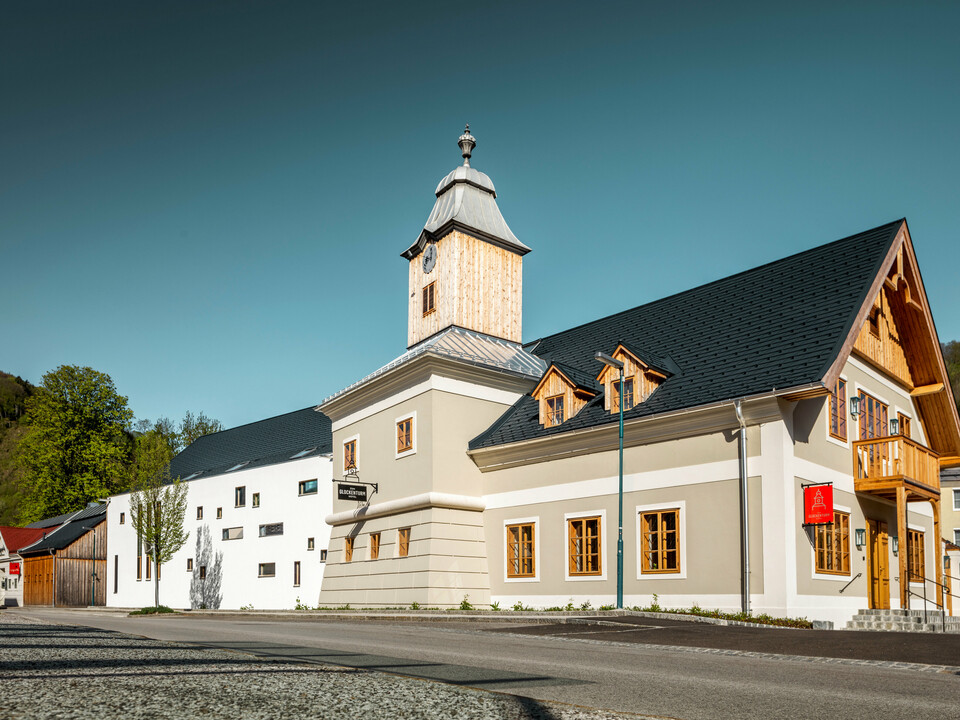 Das Dach des Hotels Glockenturm in Marktl bei Lilienfeld wurde mit der PREFA Dachschindel in P.10 Anthrazit verkleidet. Das PREFA Dachentwässerungssystem des Gebäudes ist in Naturblank gehalten. Unweit vom Hotel Glockenturm liegt das Leopold - unser Wirtshaus. Das Restaurantgebäude wurde ebenfalls mit PREFA Produkten eingedeckt.