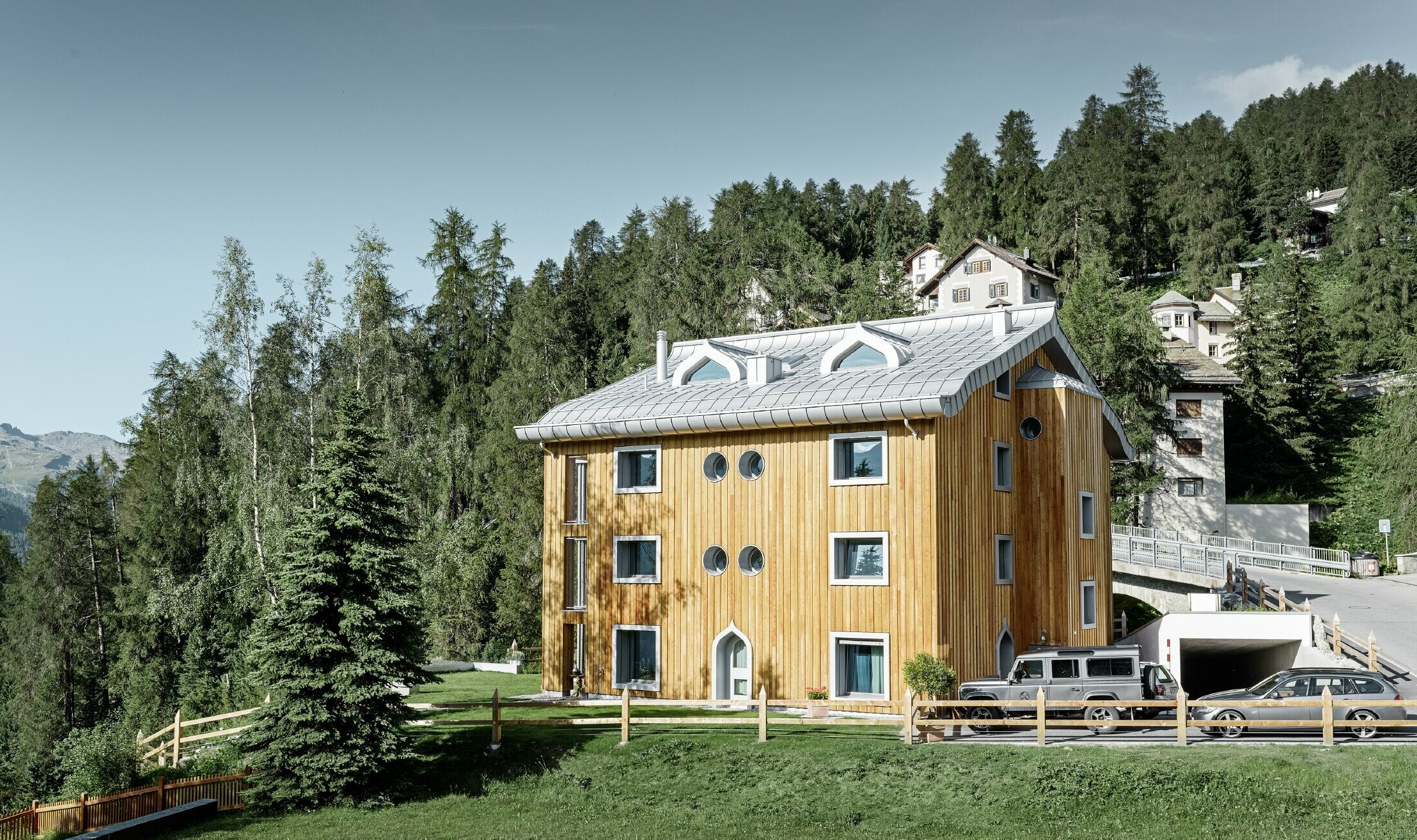 Bostadsbyggnad i St. Moritz med träfasad och aluminiumtak med svängda takskenor i silvermetallic