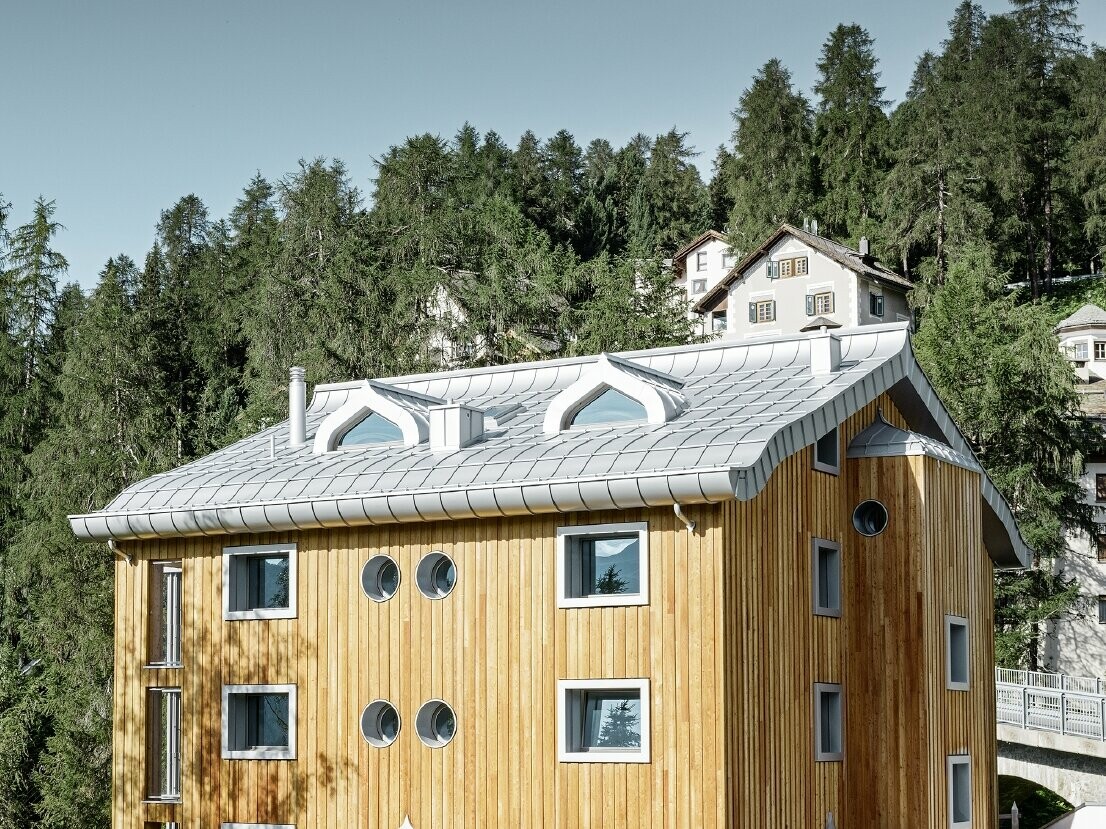 Bostadsbyggnad i St. Moritz med träfasad och aluminiumtak med svängda takskenor i silvermetallic