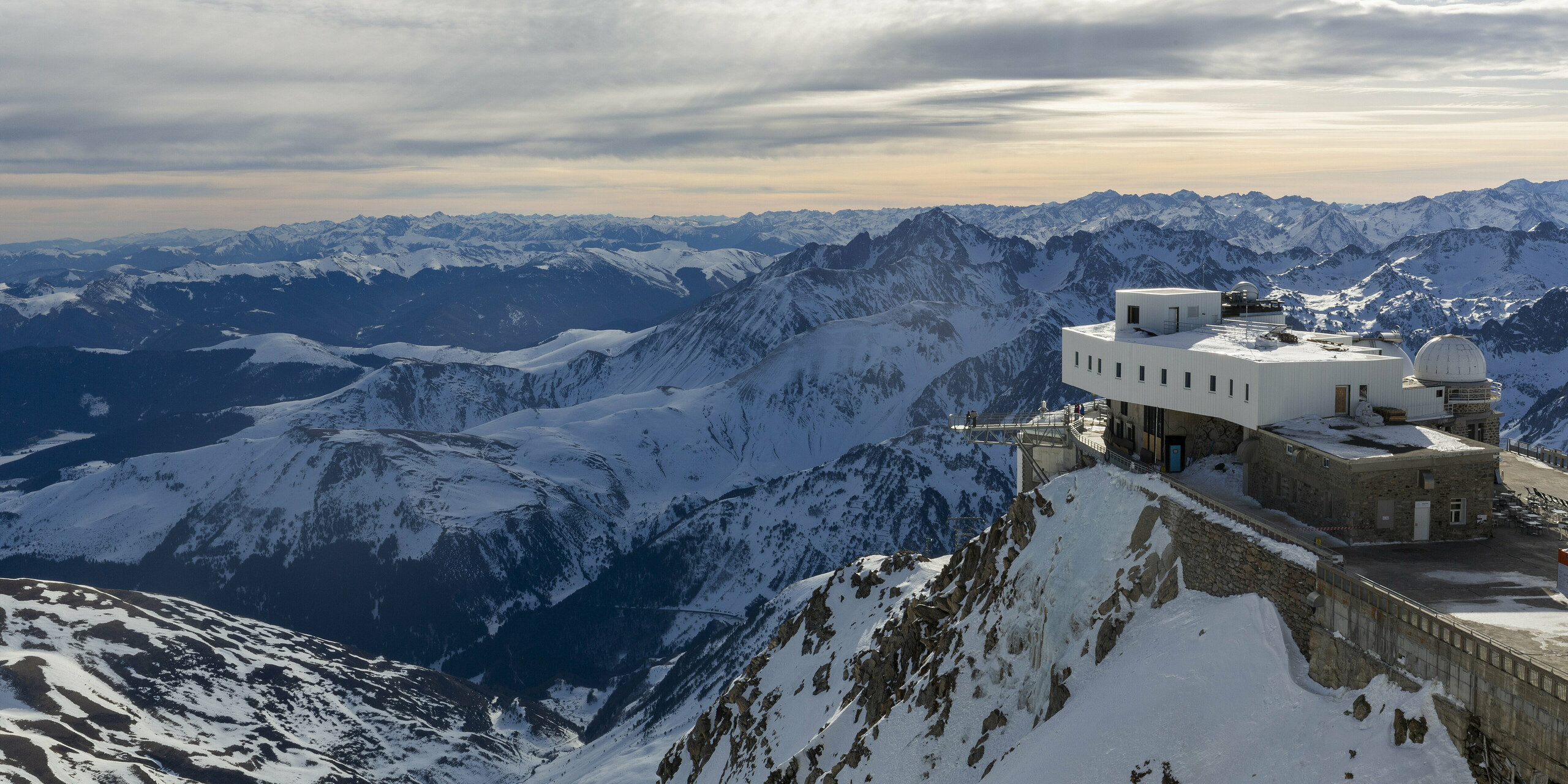 Das Midi-Pyrénées-Observatorium, hoch auf einem verschneiten Berggipfel gelegen, bietet eine atemberaubende Aussicht auf die umliegenden schneebedeckten Pyrenäen. Das Observatorium zeigt seine neue, mit PREFALZ in der Farbe P.10 Reinweiß verkleidete Fassade, die sich aufgrund der extremen Wetterbedingungen im Hochgebirge als ideal erwiesen hat. Die Wetterbeständigkeit, Korrosionsbeständigkeit und Wartungsarmut von PREFALZ waren entscheidende Faktoren für die Materialwahl. Die Bauarbeiten konnten nur in den Sommermonaten durchgeführt werden und dauerten über drei Jahre. Der leichte Transport des Materials per Hubschrauber spielte ebenfalls eine wesentliche Rolle.