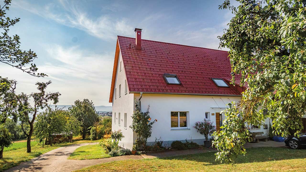 Romantiskt litet hus på landsbygden med massor av träd och buskar. Täckt med ett tak från PREFA i oxidrött.