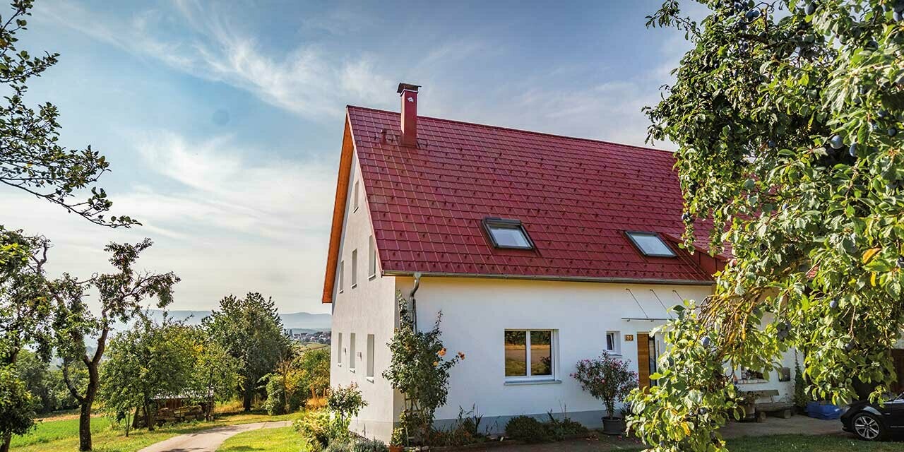 Romantiskt litet hus på landsbygden med massor av träd och buskar. Täckt med ett tak från PREFA i oxidrött.