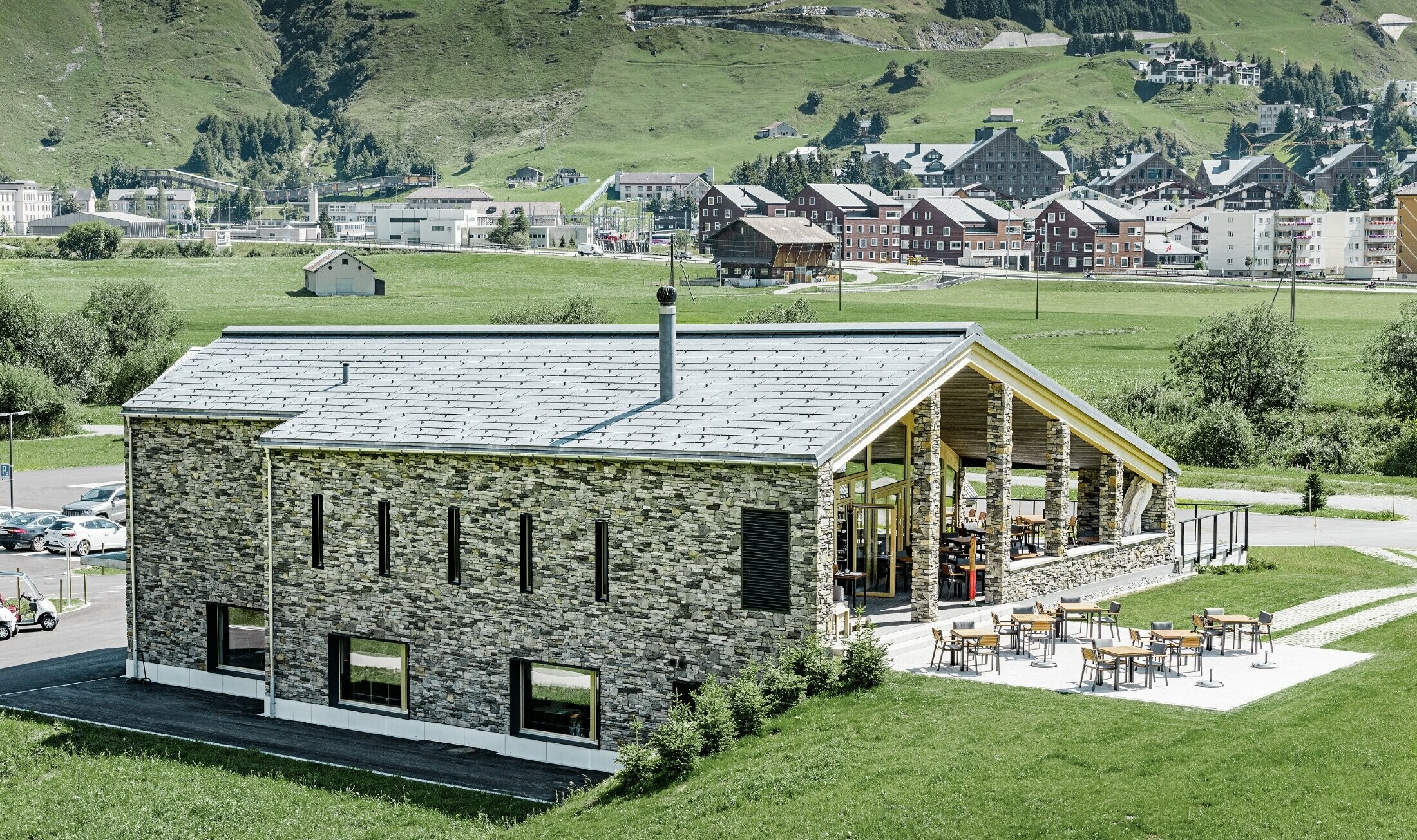 Modernt klubbhus vid golfbanan i Andermatt med stenfasad och PREFA:s takpanel FX.12 av aluminium i stengrått