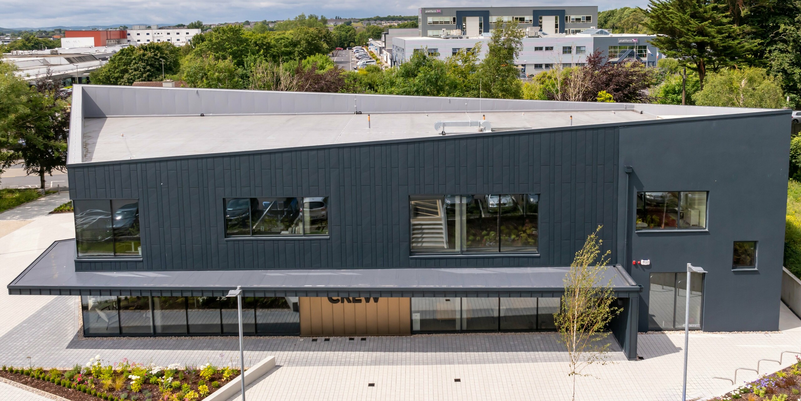 Vogelperspektive des CREW-Gebäudes in Galway, Irland, mit einer modernen Fassade aus PREFA Siding.X Fassadenpaneelen und PREFALZ in P.10 Anthrazit. Die schrägen Dachlinien und die klar strukturierten Fensterflächen betonen das innovative Design des Gebäudes. Die anthrazitfarbene Aluminiumverkleidung harmoniert mit der Umgebung und verleiht dem Gebäude ein zeitgemäßes, hochwertiges Erscheinungsbild.