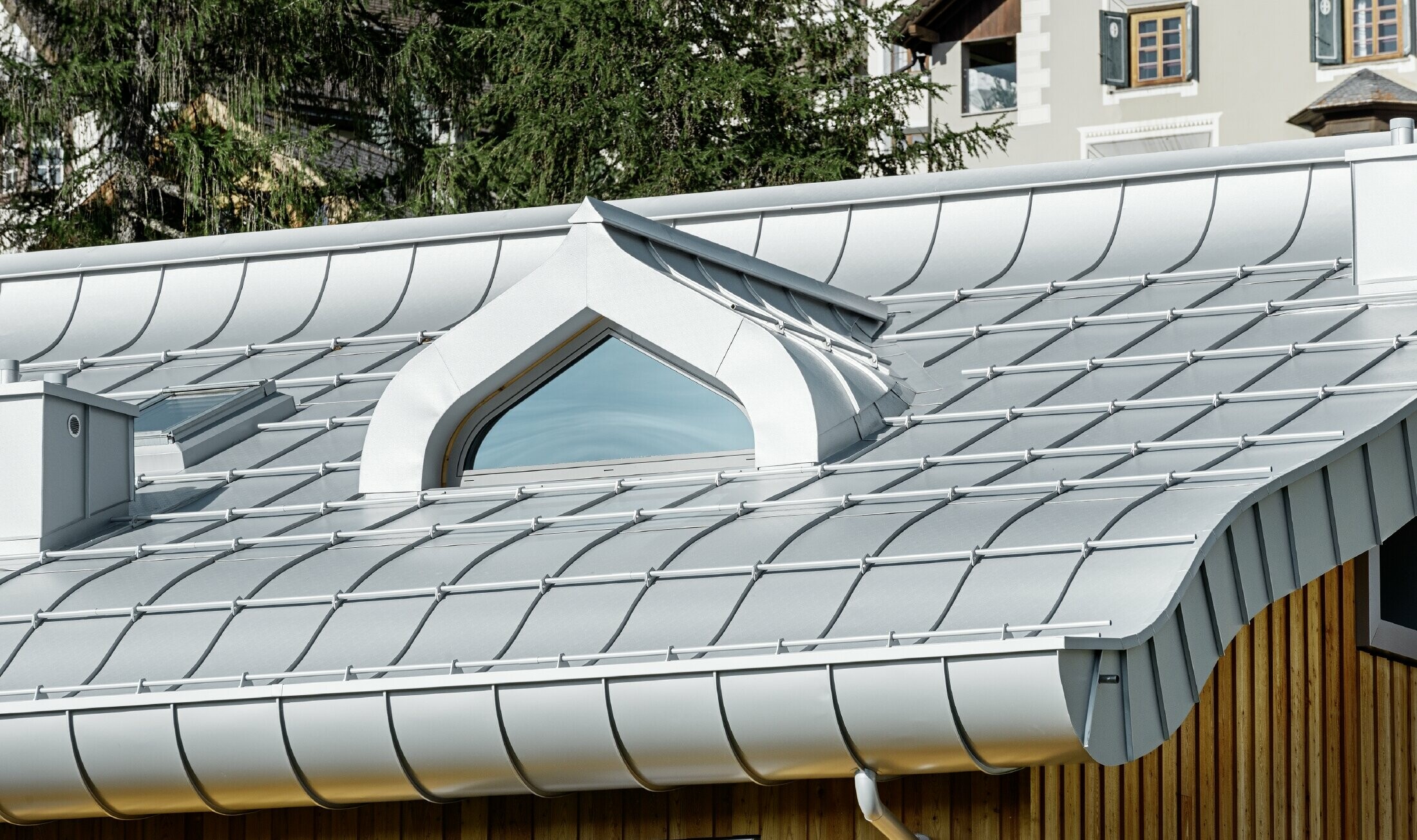 Bostadsbyggnad i St. Moritz med träfasad och aluminiumtak med svängda takskenor i silvermetallic