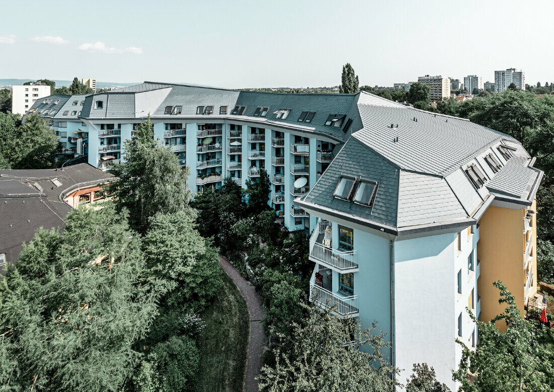 Stort bostadshus för äldreomsorg, täckt med PREFA takshingel och Prefalz i stengrått, med många balkonger.