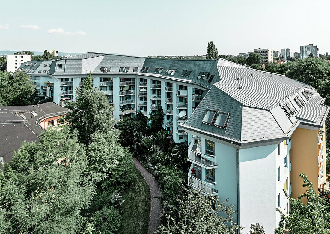 Stort bostadshus för äldreomsorg, täckt med PREFA takshingel och Prefalz i stengrått, med många balkonger.